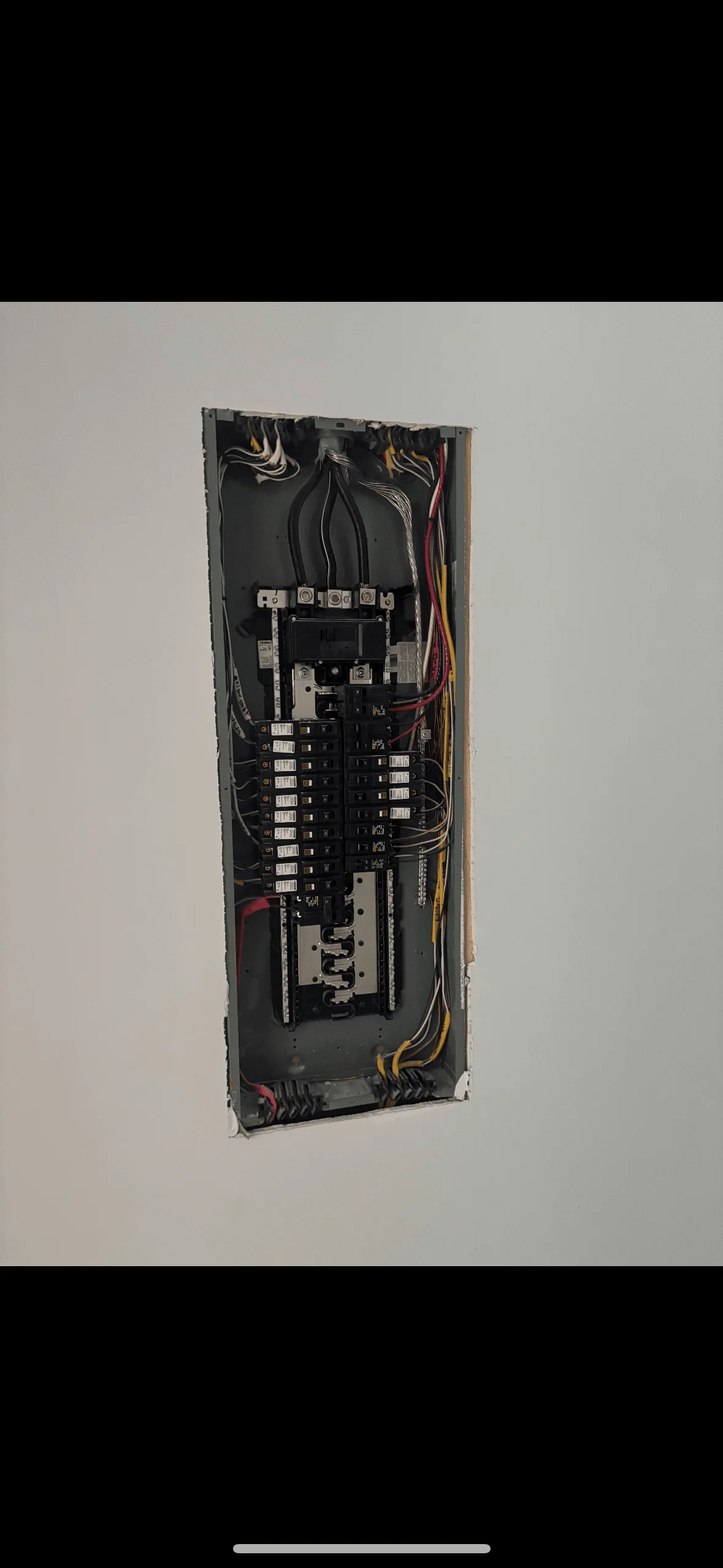 An open electrical panel with circuit breakers and wiring in an interior wall installation.