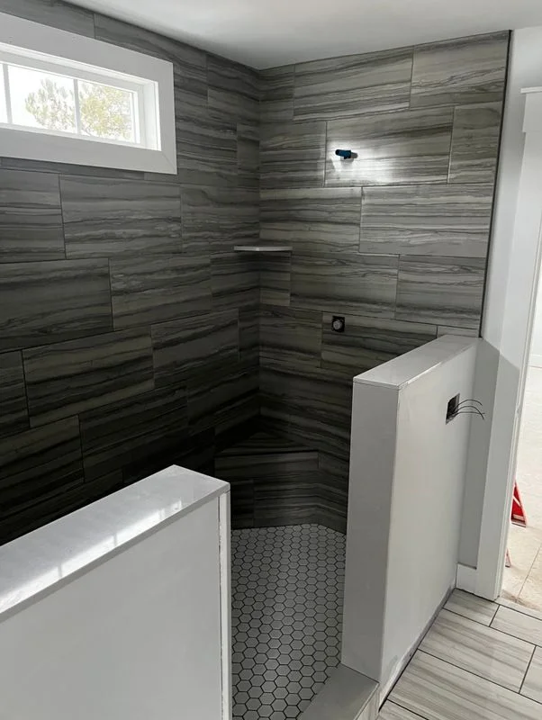 A bathroom remodel featuring a walk-in shower with dark wood-grain tile walls and hexagonal floor tile in a modern residential bathroom.