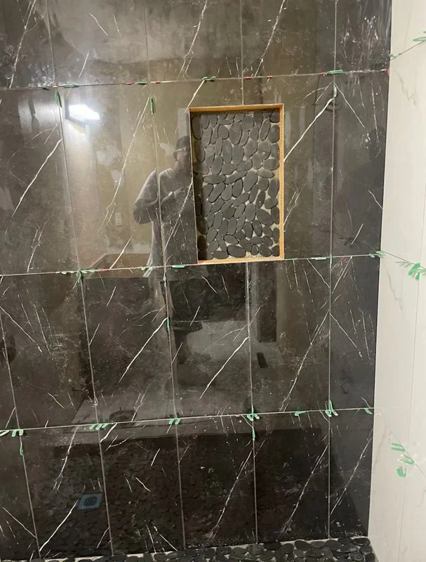 Bathroom tile installation in progress with dark marble-look tiles and a decorative accent niche in a renovation project.