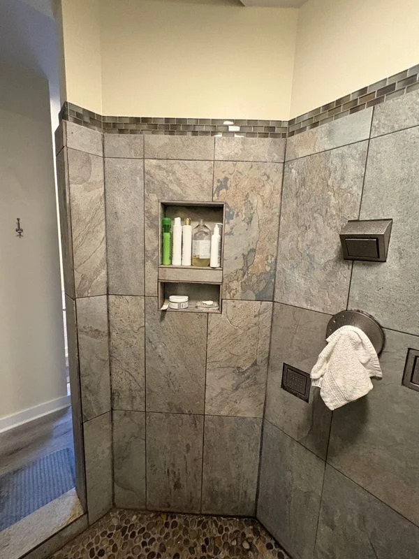 Custom tile shower with built-in niche and mosaic floor in a residential bathroom remodel.
