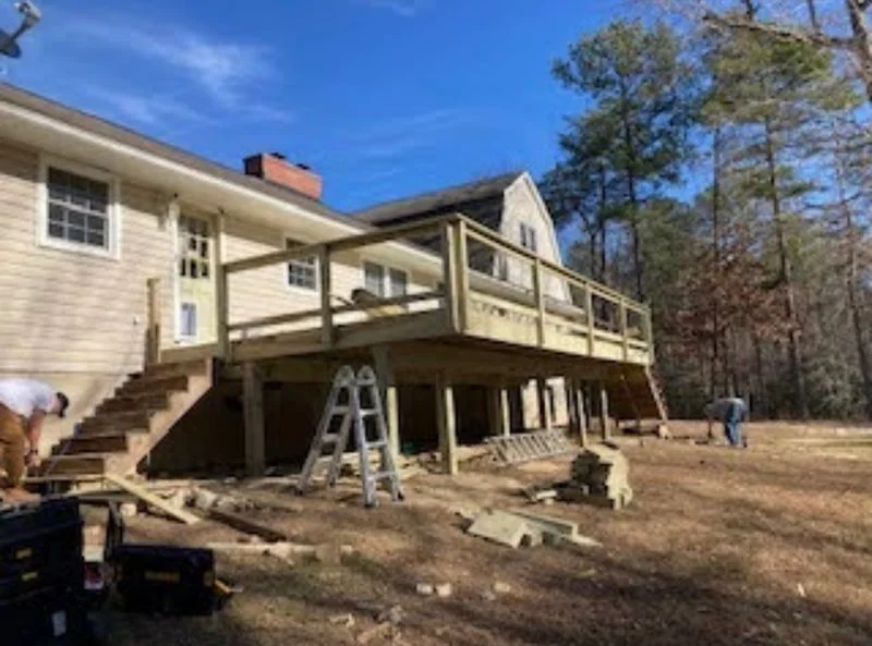 A deck and covered porch addition under construction on a residential home in a wooded setting.