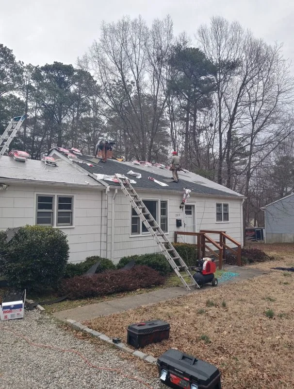 Roof replacement work in progress on a white single-family home with workers and equipment on the roof.