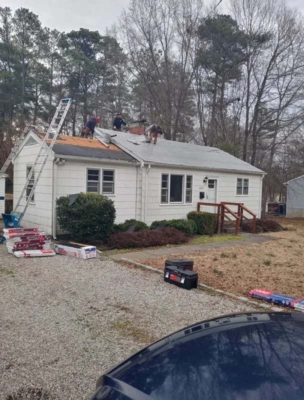 Roof replacement work in progress on a white single-story residential home with workers and equipment visible on the roof.