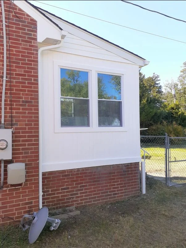 A white vinyl-clad room addition with double-hung windows attached to a red brick home exterior.