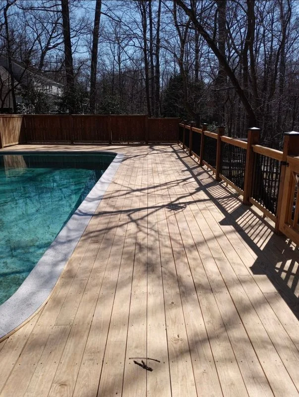 A wooden deck with pool surround and railings in a wooded residential setting.