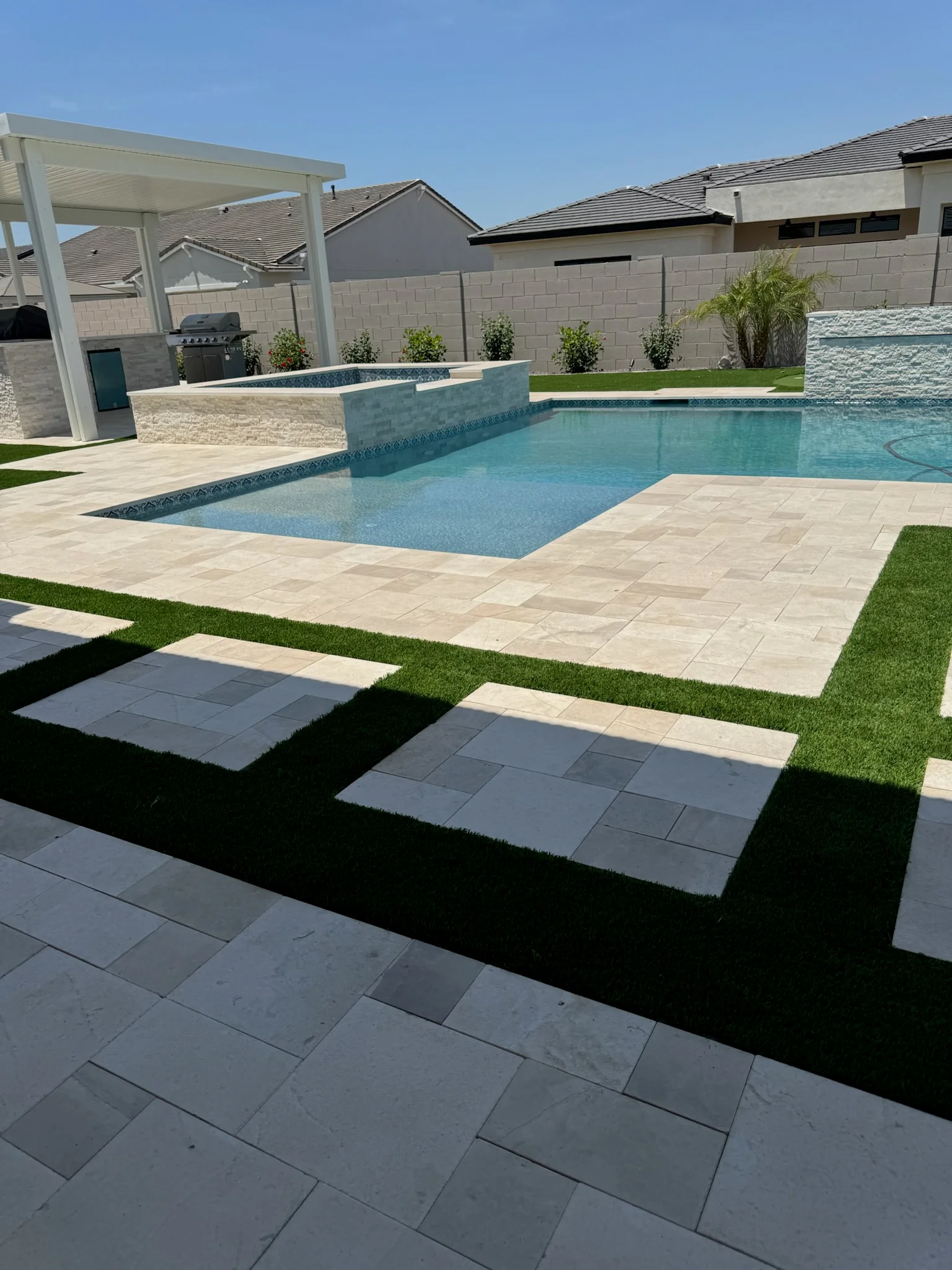 Custom swimming pool with decorative tile border and integrated spa in a modern residential backyard with patio and pergola