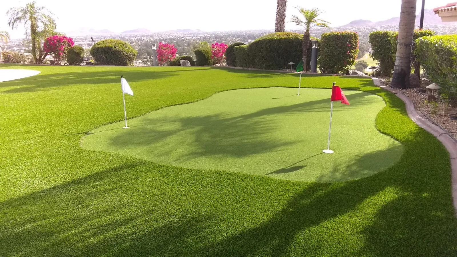 A private putting green with multiple flag holes in a luxurious residential backyard overlooking a sprawling city valley.