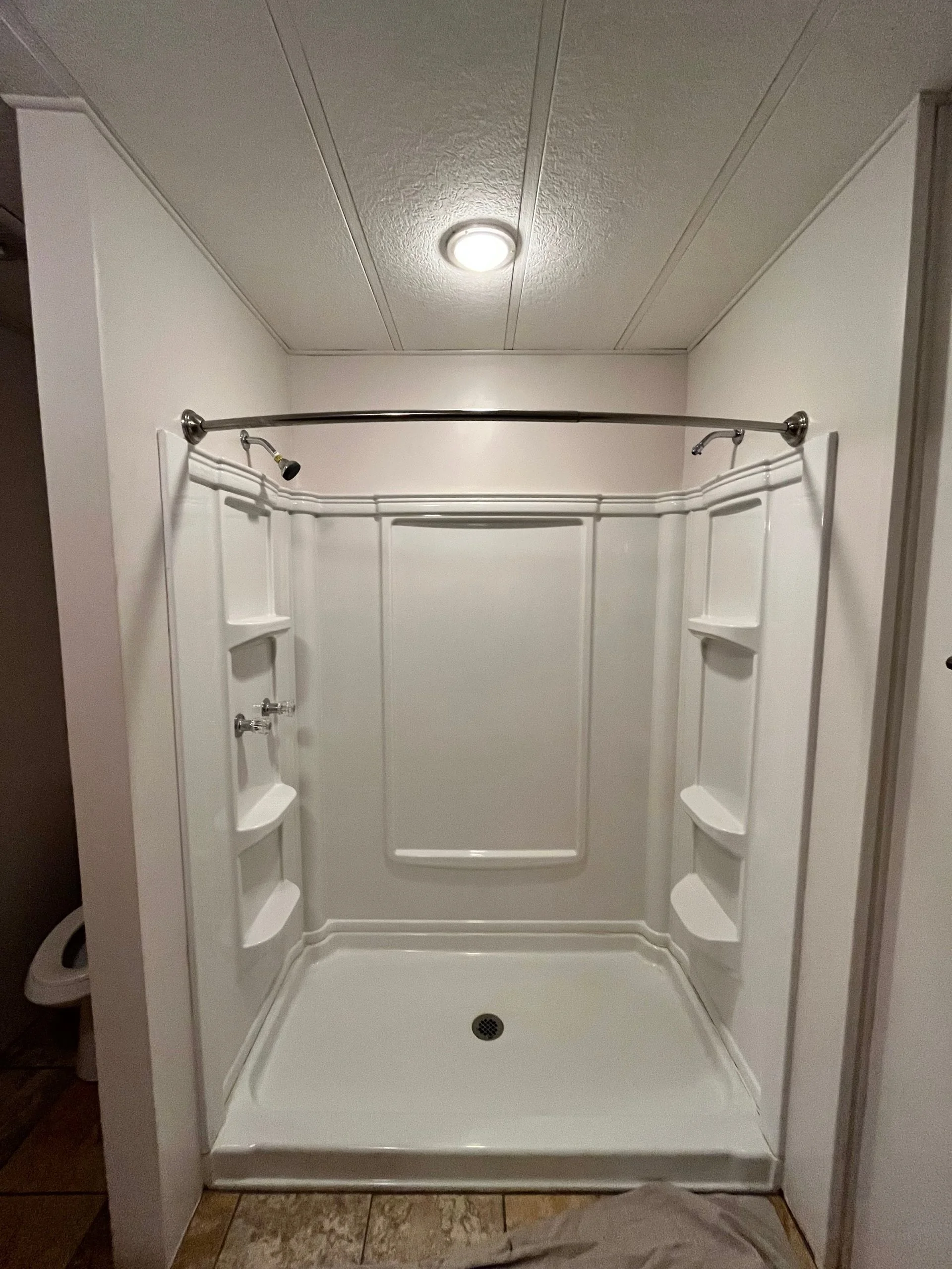 Modern white walk-in shower stall with integrated shelving and a chrome curved curtain rod.