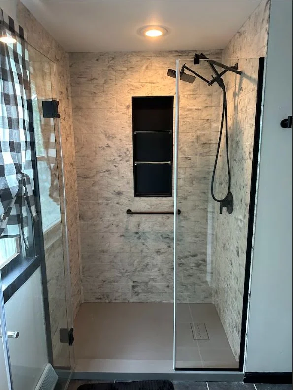 Modern walk-in shower featuring marble-look wall tiles, black hardware, and a glass partition.