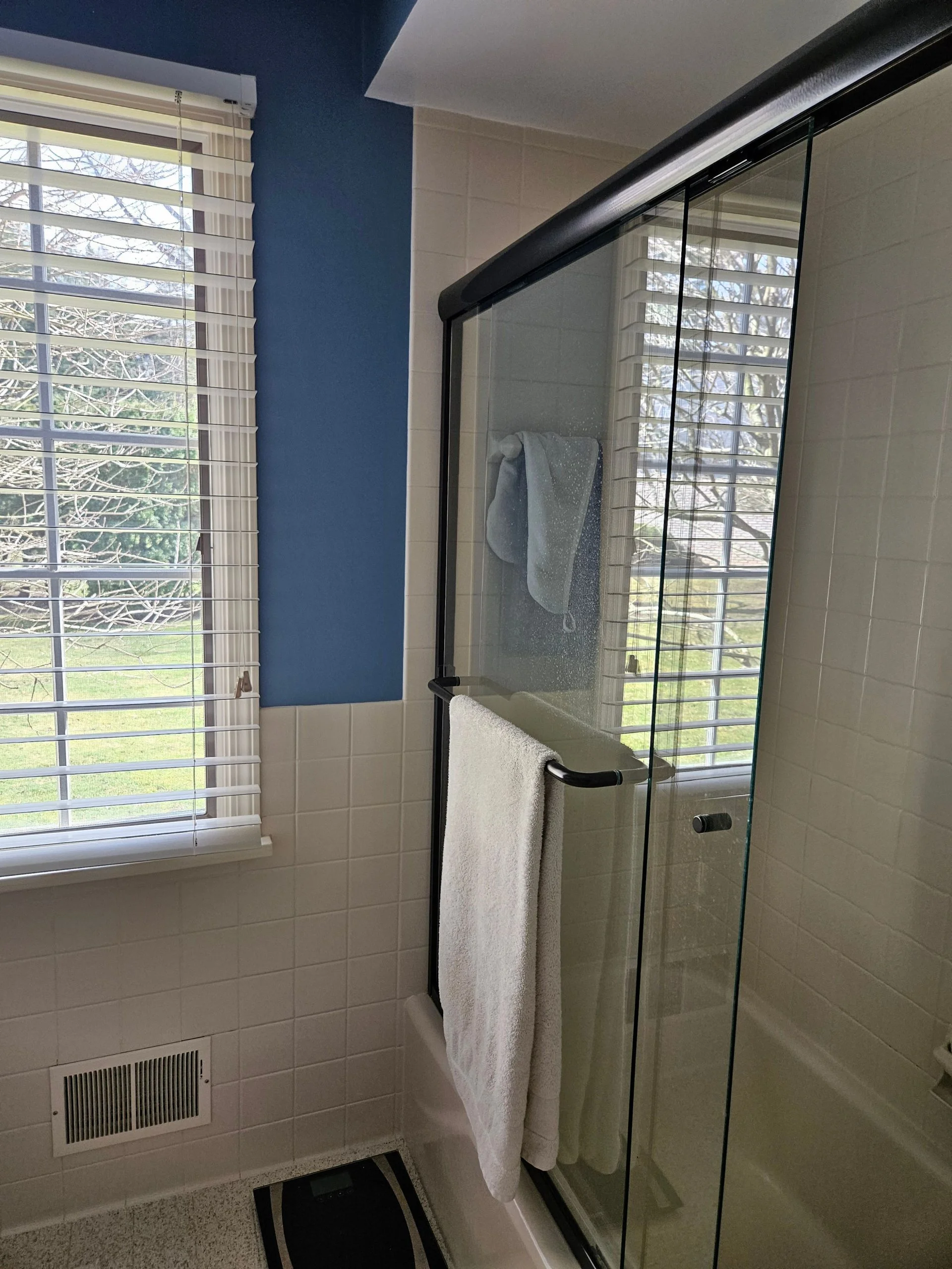 Modern sliding glass shower door with black frame and white tile bathroom walls.