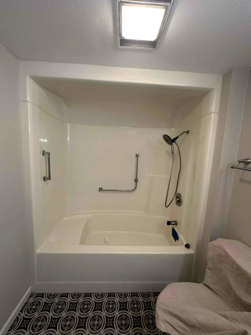 White acrylic bathtub and shower surround with safety grab bars and handheld shower head.
