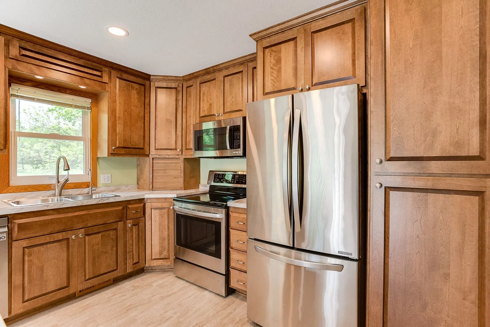 Modern kitchen featuring honey oak cabinets, stainless steel appliances, and a double sink near a window.