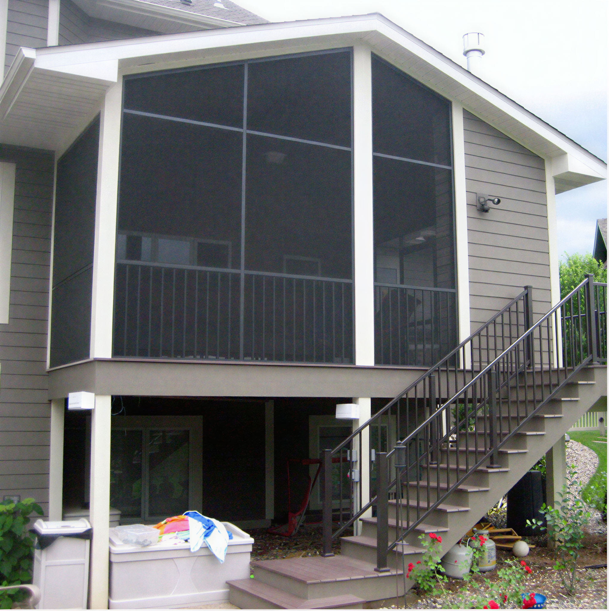 Elevated screened-in porch featuring gray lap siding and a staircase with black metal railings.