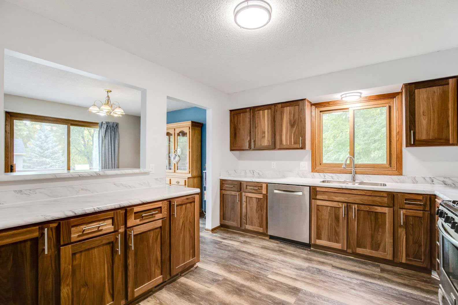 Modern kitchen remodel featuring walnut cabinets, white marble countertops, and stainless steel dishwasher.