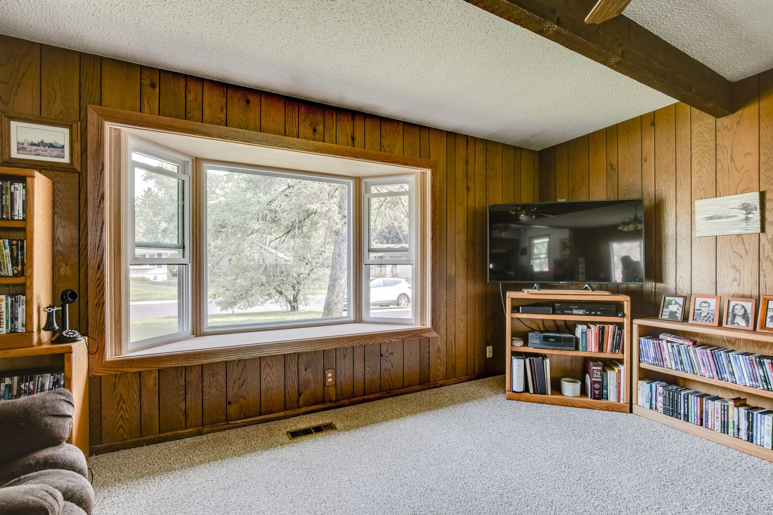 Large bay window with wood frame installed in a living room with wood paneling walls.
