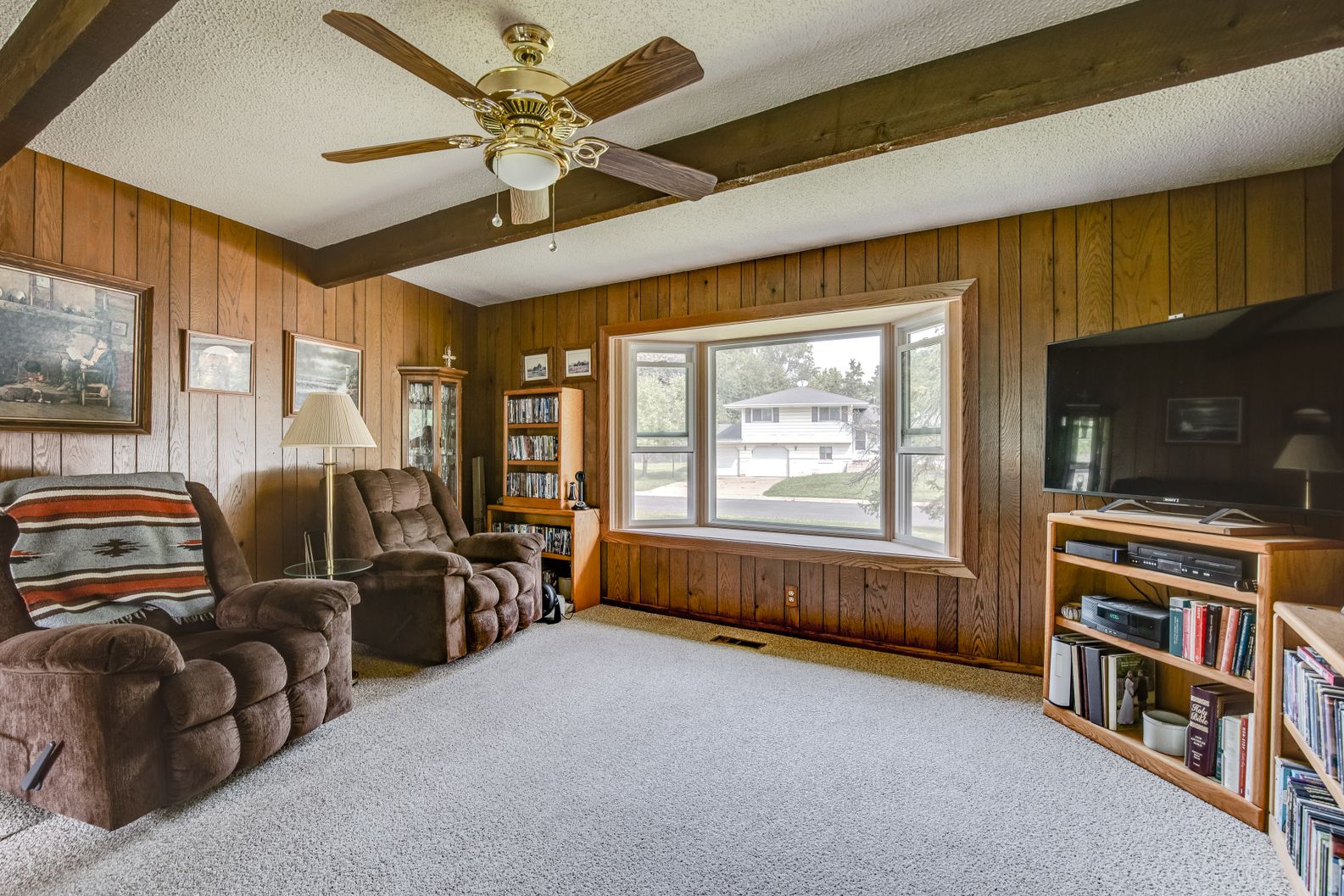 Wood paneled interior living room with a large bay window and exposed dark wooden ceiling beams.