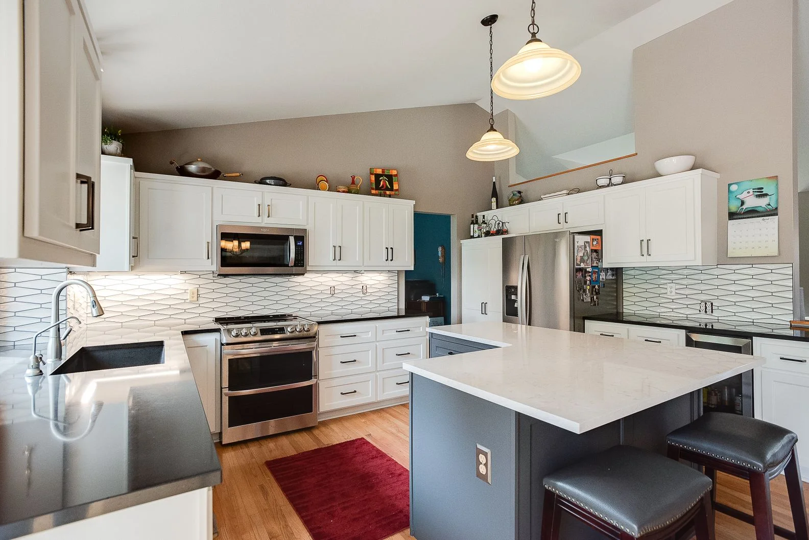 Modern kitchen remodel featuring white upper cabinets, a grey island, and white elongated hexagonal tile backsplash.