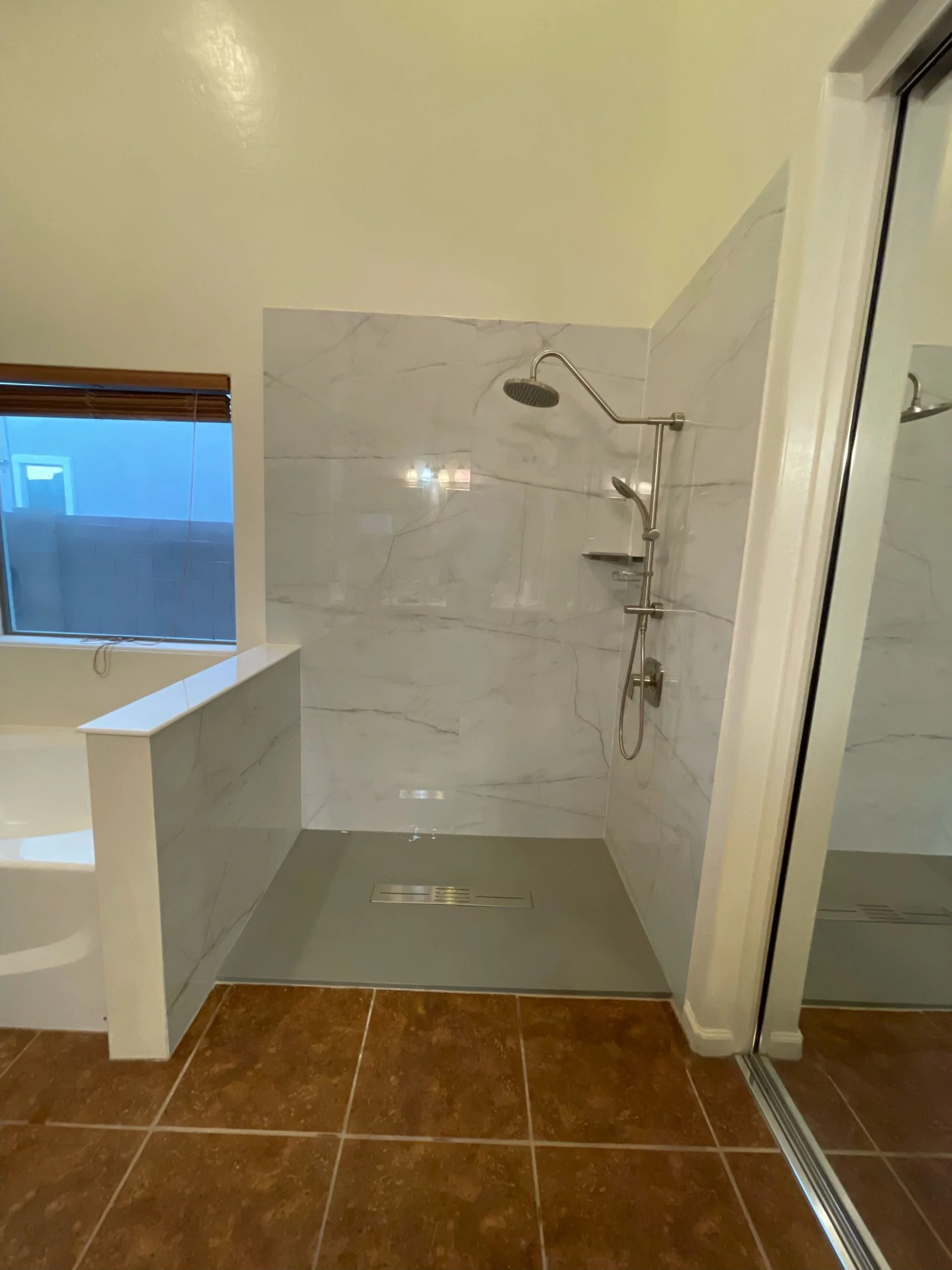 Modern walk-in shower featuring marble pattern wall tiles, a gray base, and chrome fixtures.