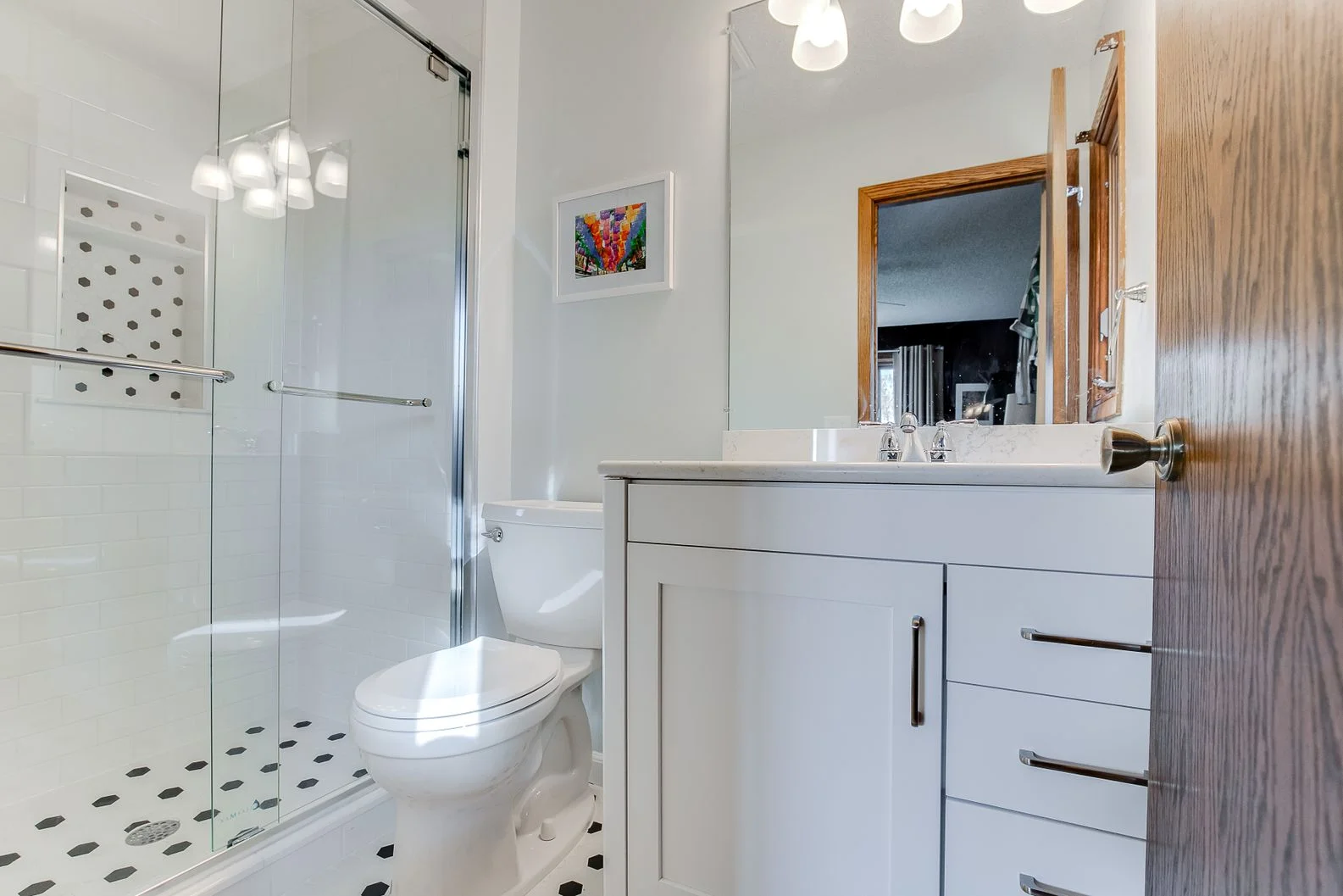 Modern bathroom featuring white shaker vanity, glass walk-in shower, and black and white honeycomb tile.