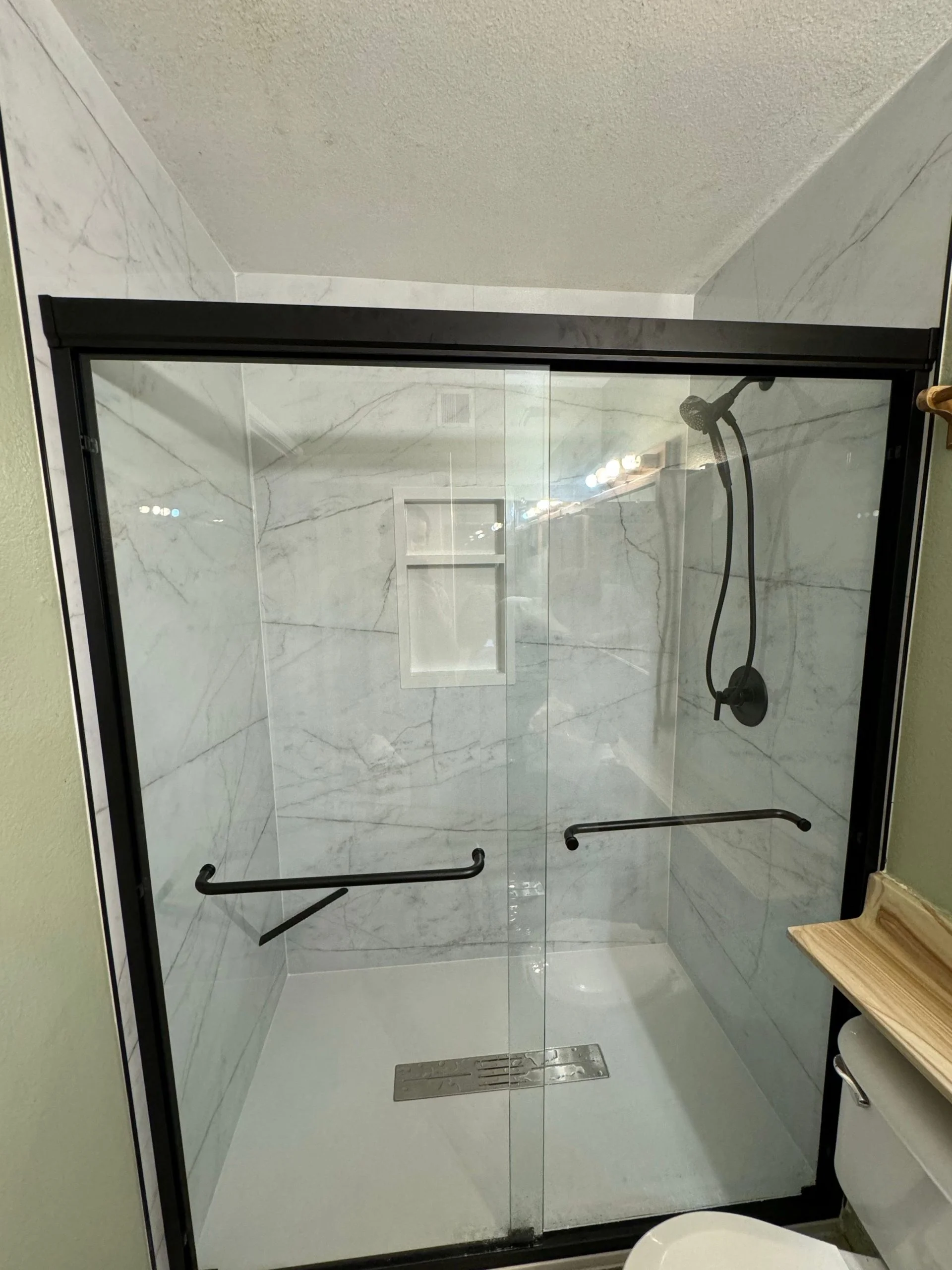 Modern walk-in shower featuring marble-patterned tile walls and black frame sliding glass doors.