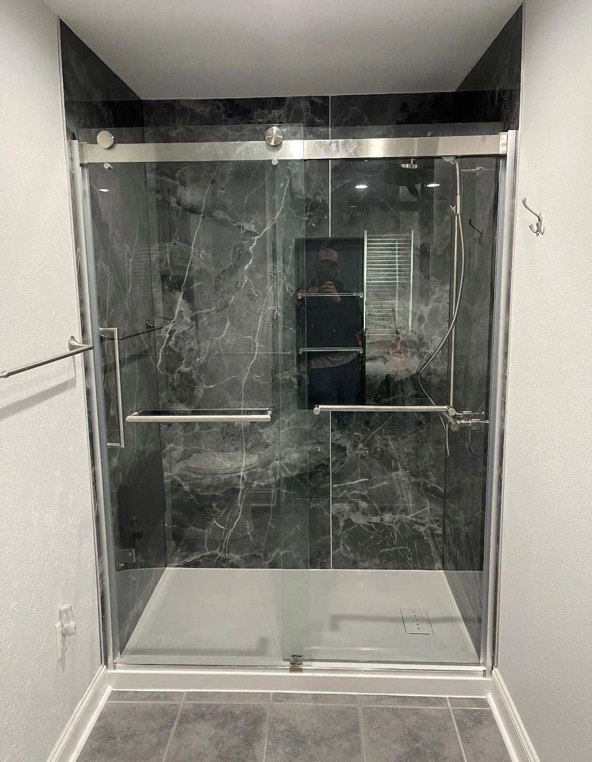 Modern glass walk-in shower with dark gray marble-patterned wall surround and chrome sliding hardware.