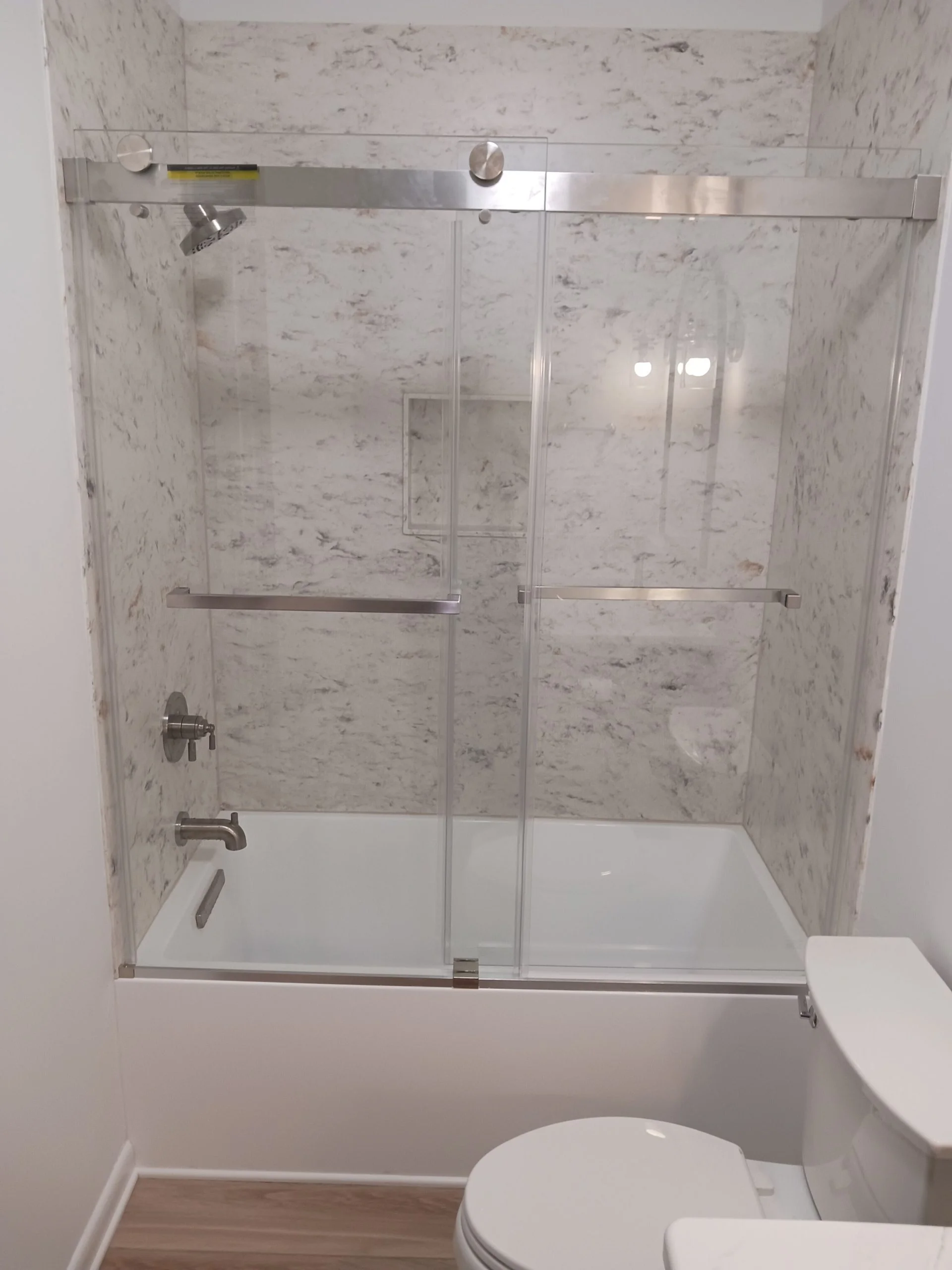 Modern bathtub and shower combination with sliding glass doors and marble-patterned wall surround
