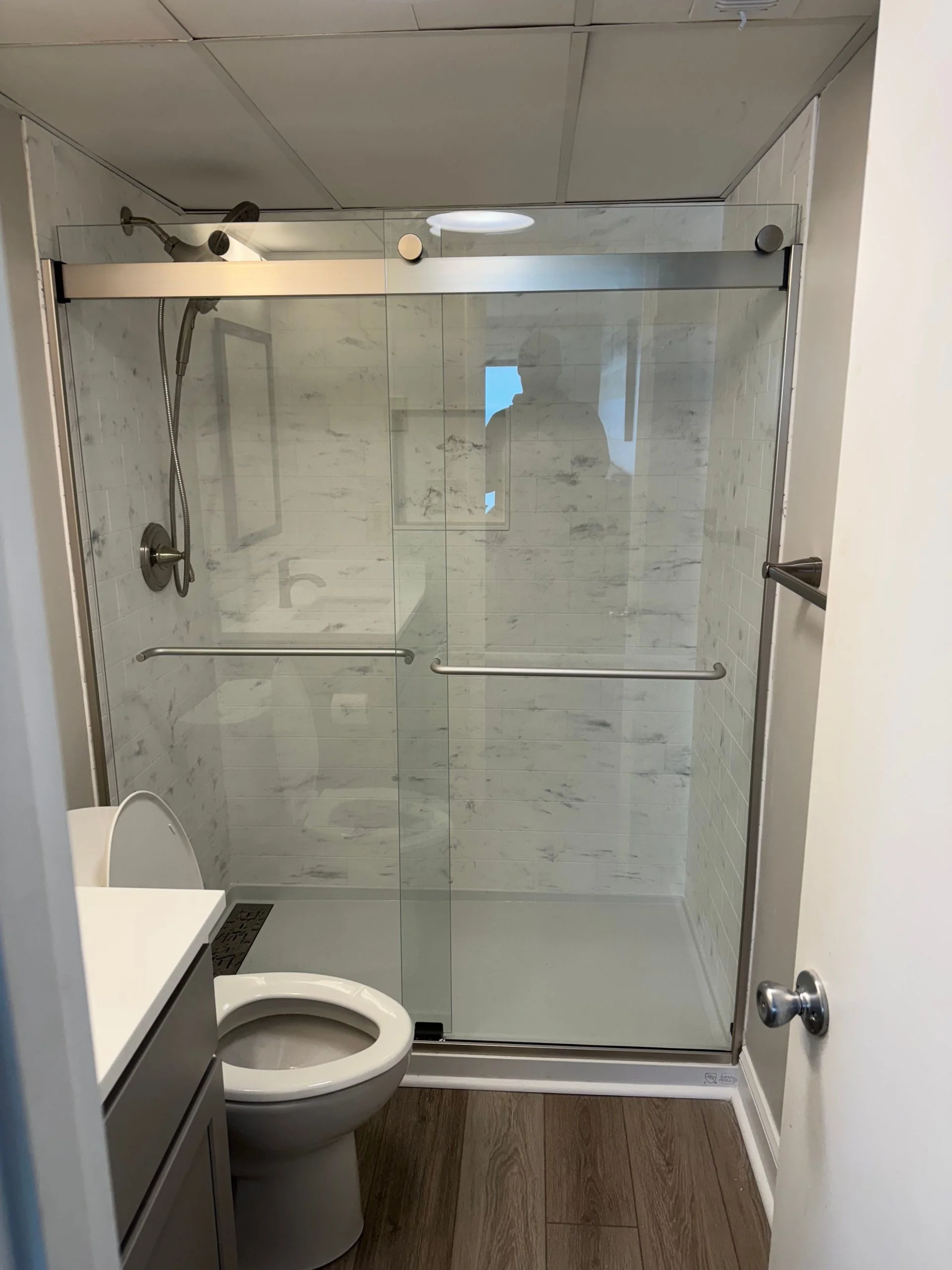 Modern walk-in shower with sliding glass doors and white marble-patterned subway tiles.