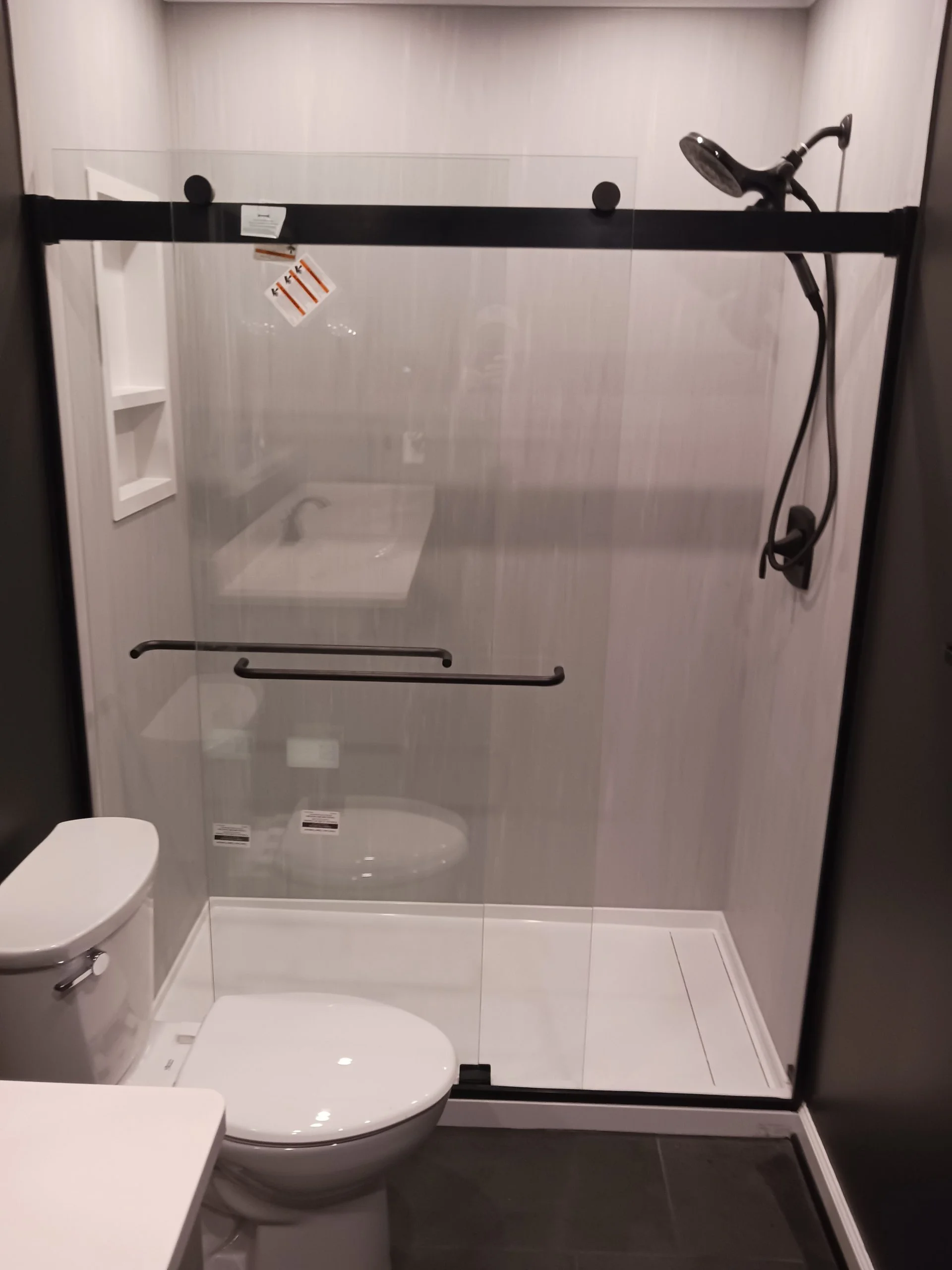 Modern walk-in shower with sliding glass doors, black hardware, and a white toilet in foreground.