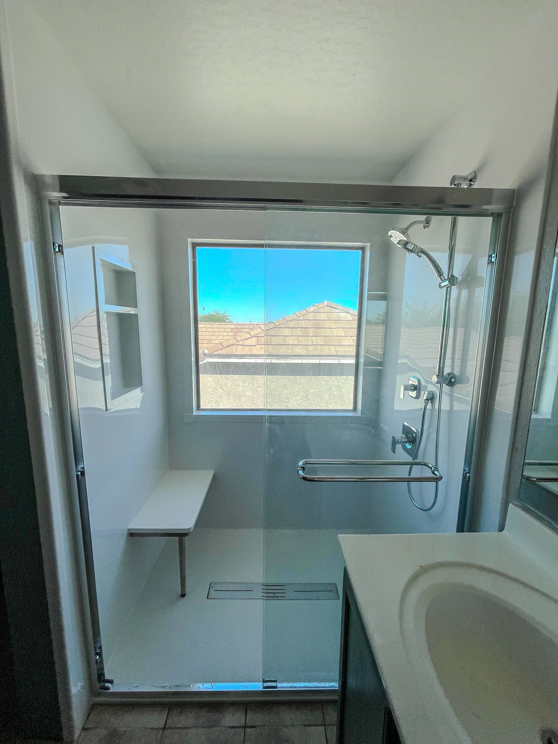 Modern walk-in shower with sliding glass doors, a built-in bench, and a large window.