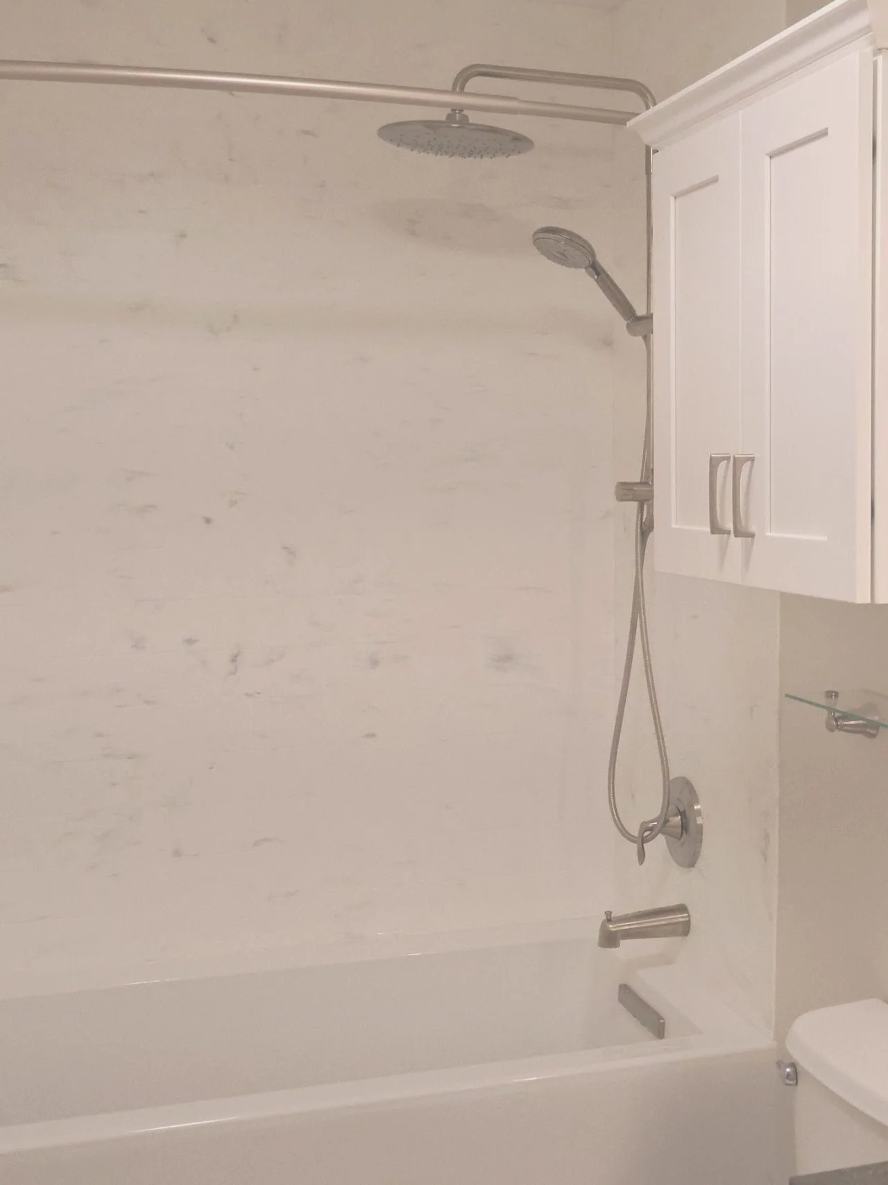 Modern white marble shower surround with brushed nickel dual showerheads and a white shaker cabinet.