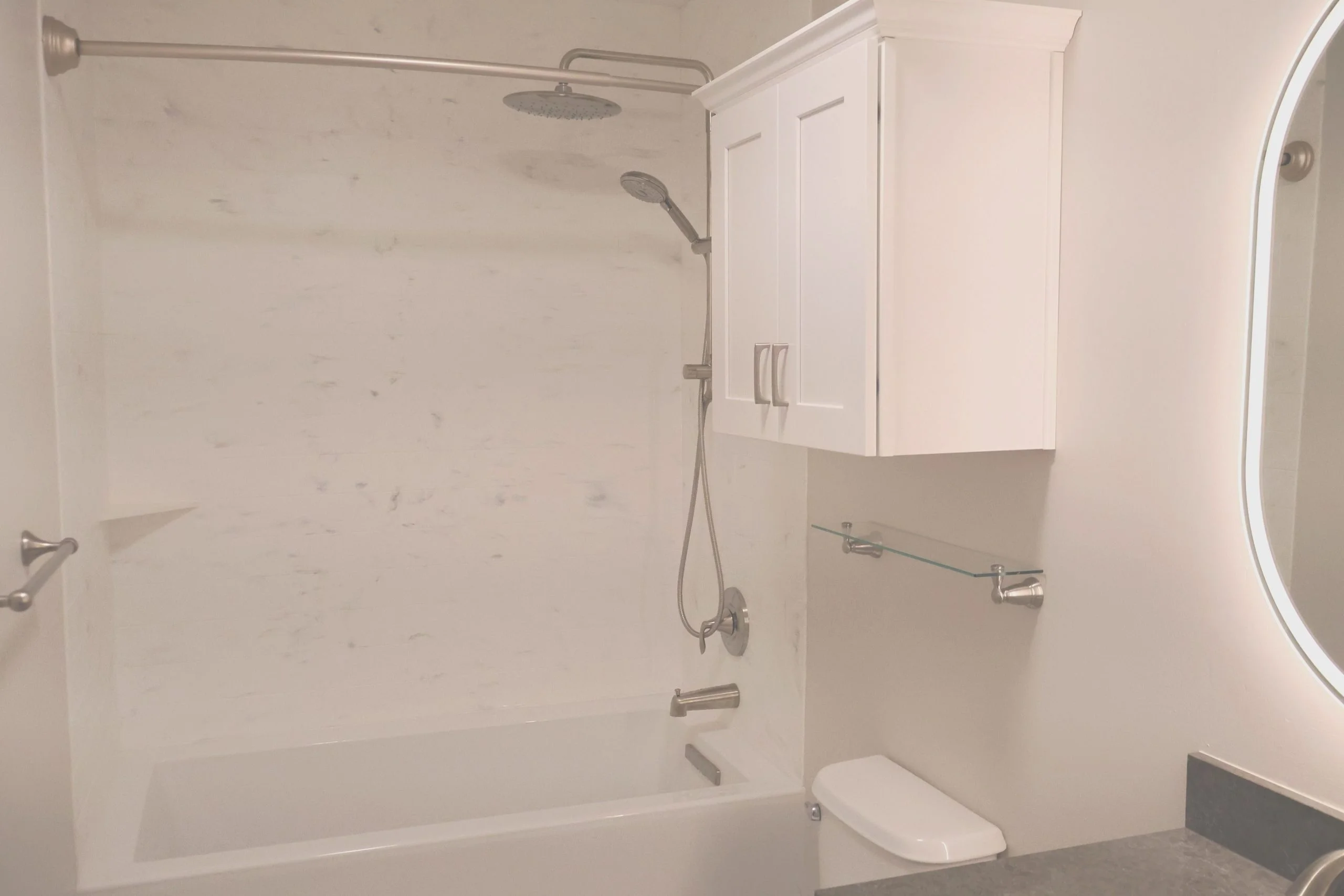 Modern white bathroom featuring a bathtub with marble wall panels and brushed nickel fixtures.