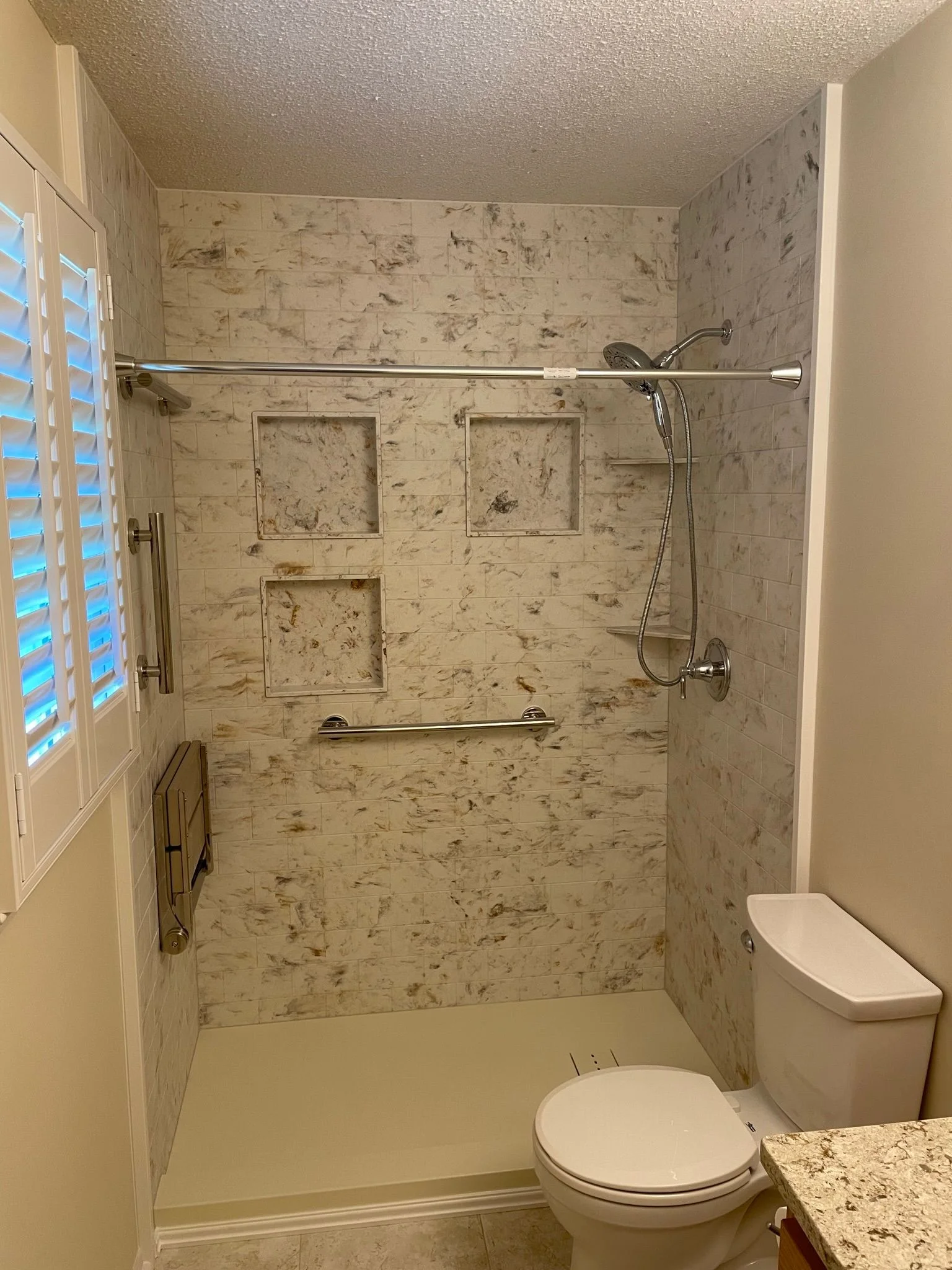 Modern walk-in shower with marbled tile, three recessed wall niches, and chrome safety grab bars.