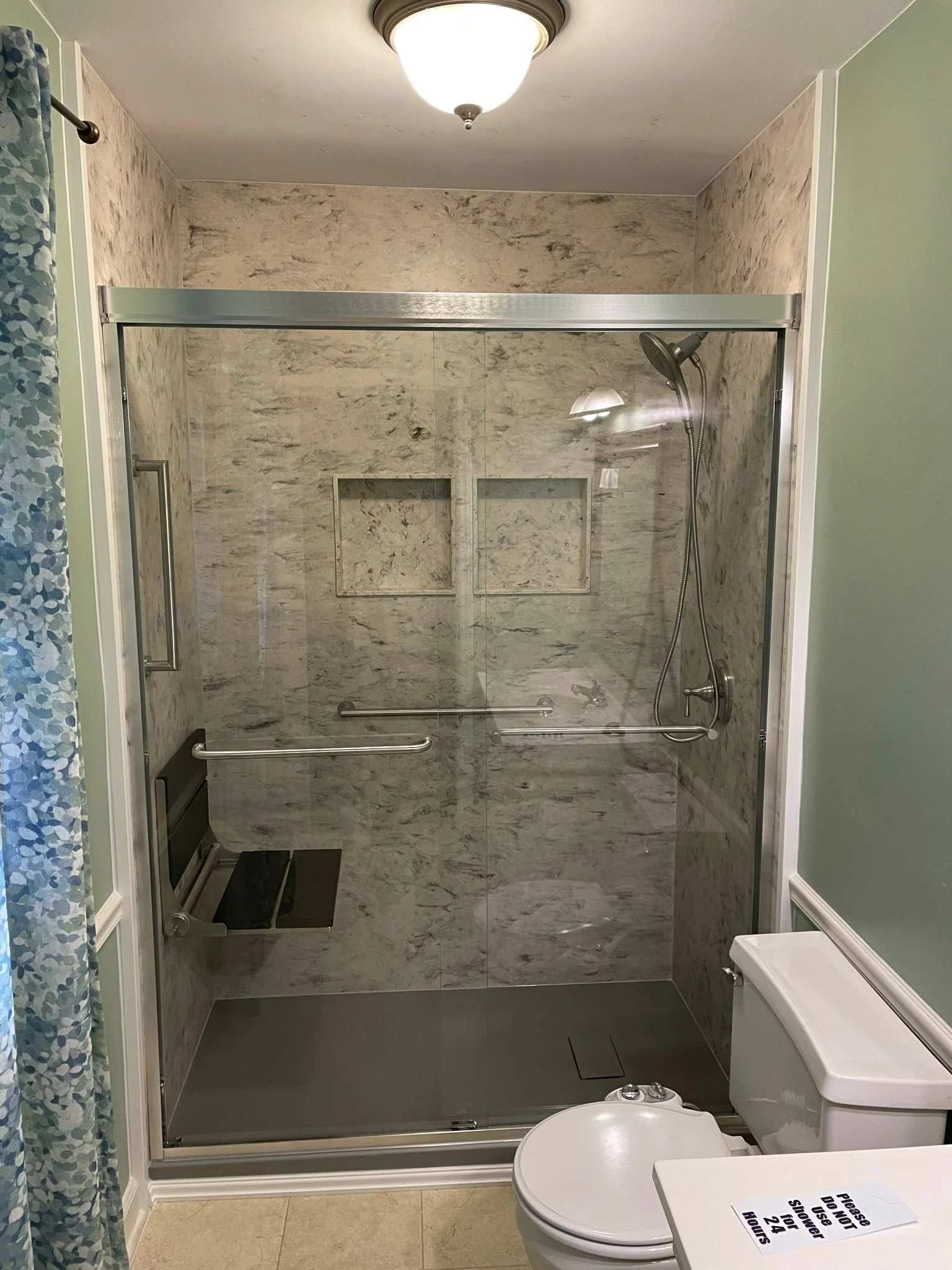 Modern walk-in shower with sliding glass doors, marble-patterned wall panels, and built-in folding seat.