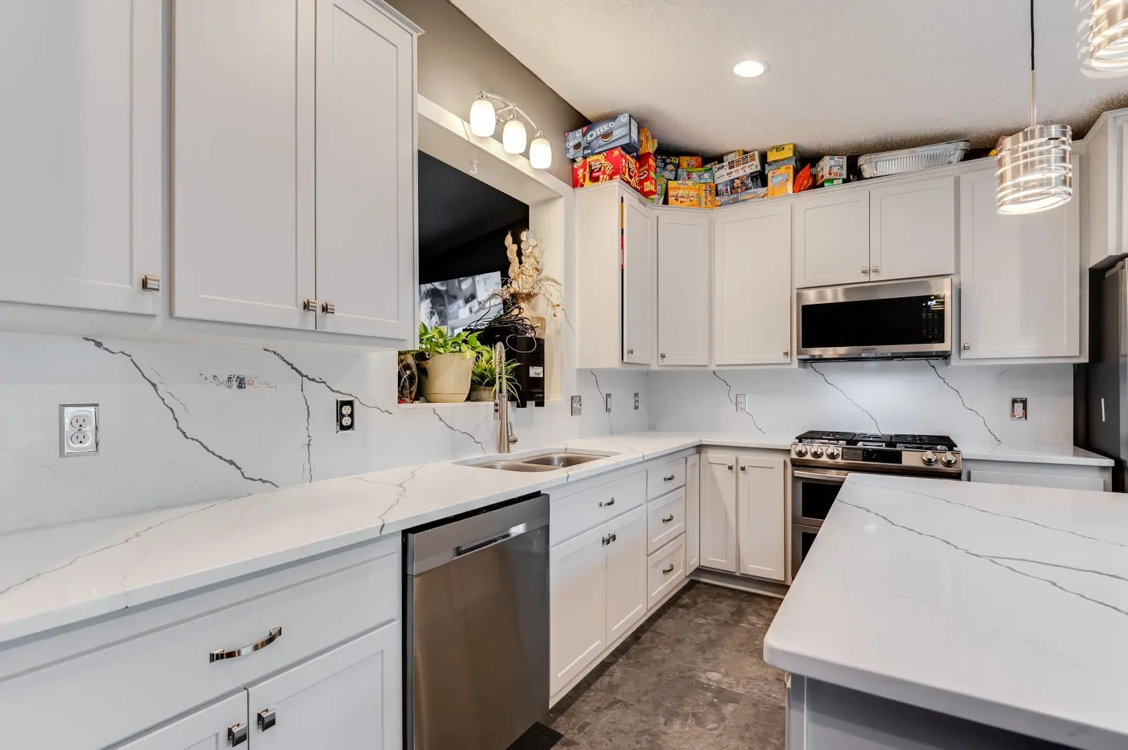 Modern kitchen with white shaker cabinets, marbled quartz countertops, and stainless steel appliances.