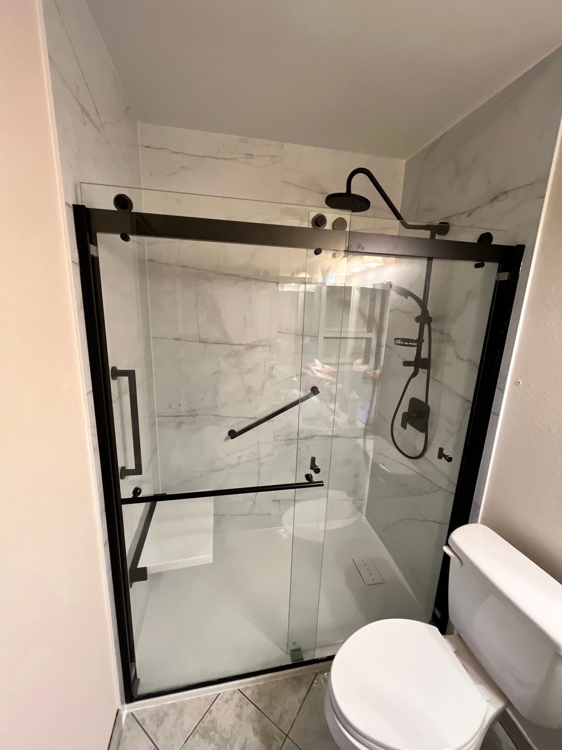 Modern walk-in shower with sliding glass doors, black hardware, and marble-patterned tile walls.