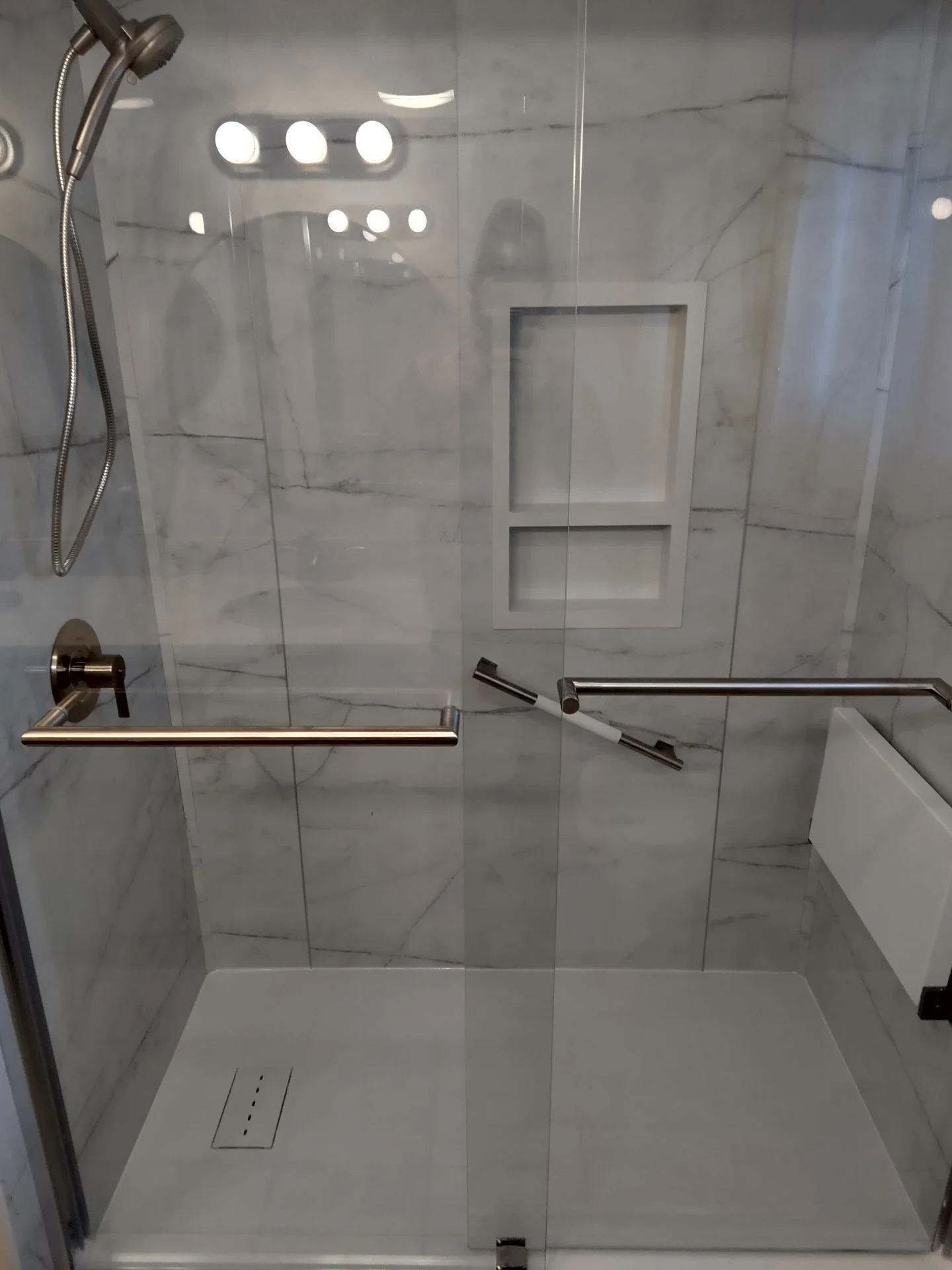 Modern walk-in shower with marble-patterned tile, glass sliding doors, and stainless steel safety grab bars.