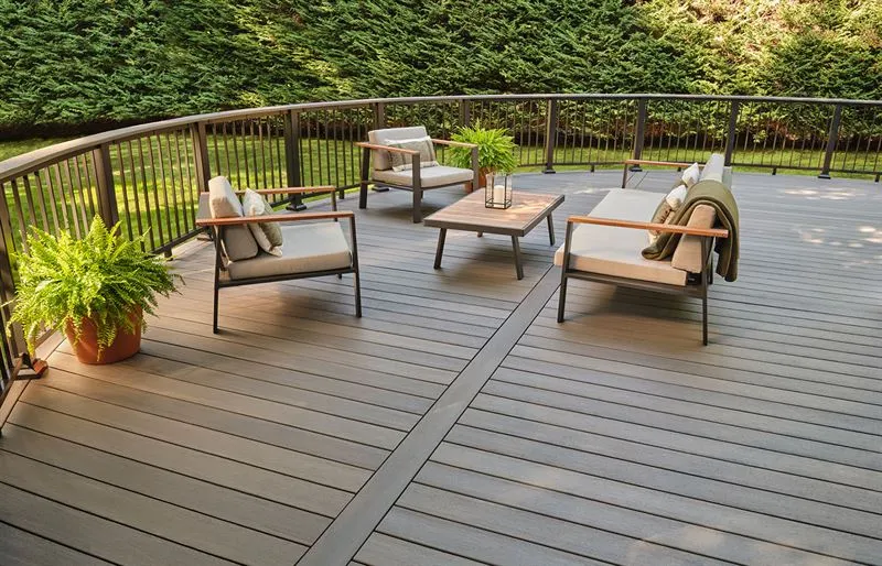 Modern curved composite deck with black metal railing, outdoor sofa, and grey lounge chairs