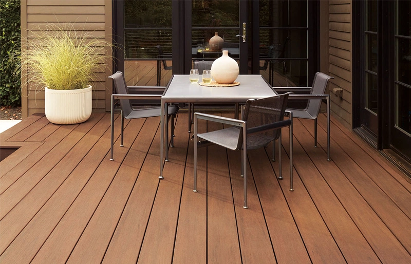 Modern composite wood deck featuring a dining table, black chairs, and brown siding background