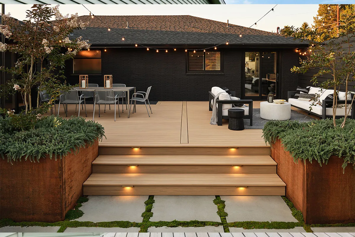 Modern composite deck with integrated stair lighting against a black brick house exterior at dusk.