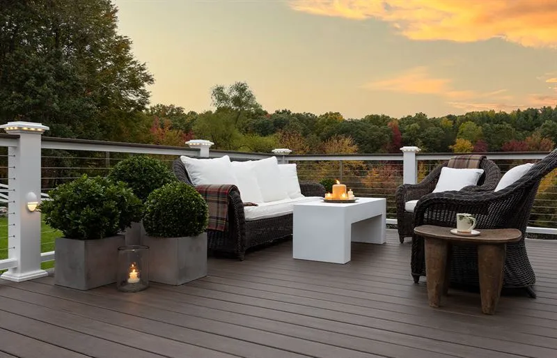 Modern composite deck with wicker furniture and cable railing overlooking a forest at sunset.