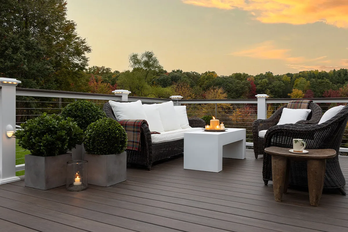 Modern composite deck featuring white railings with built-in lighting and wicker outdoor furniture at sunset.