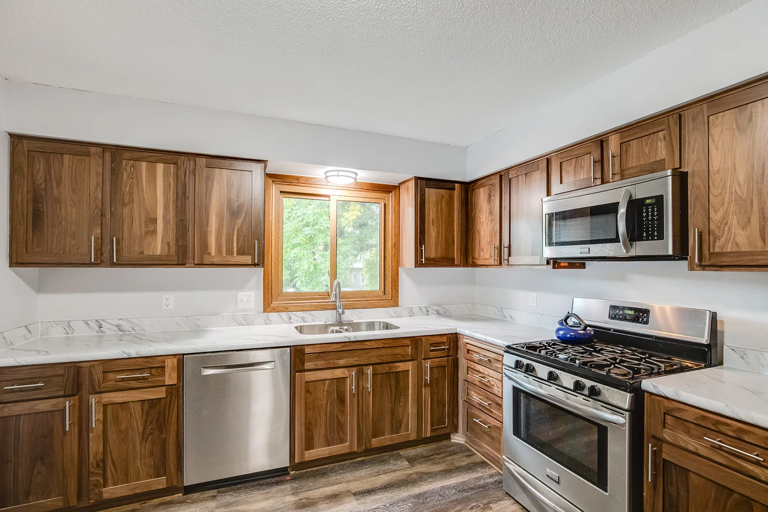 Modern kitchen featuring walnut cabinets, marble countertops, and stainless steel appliances with a window view.