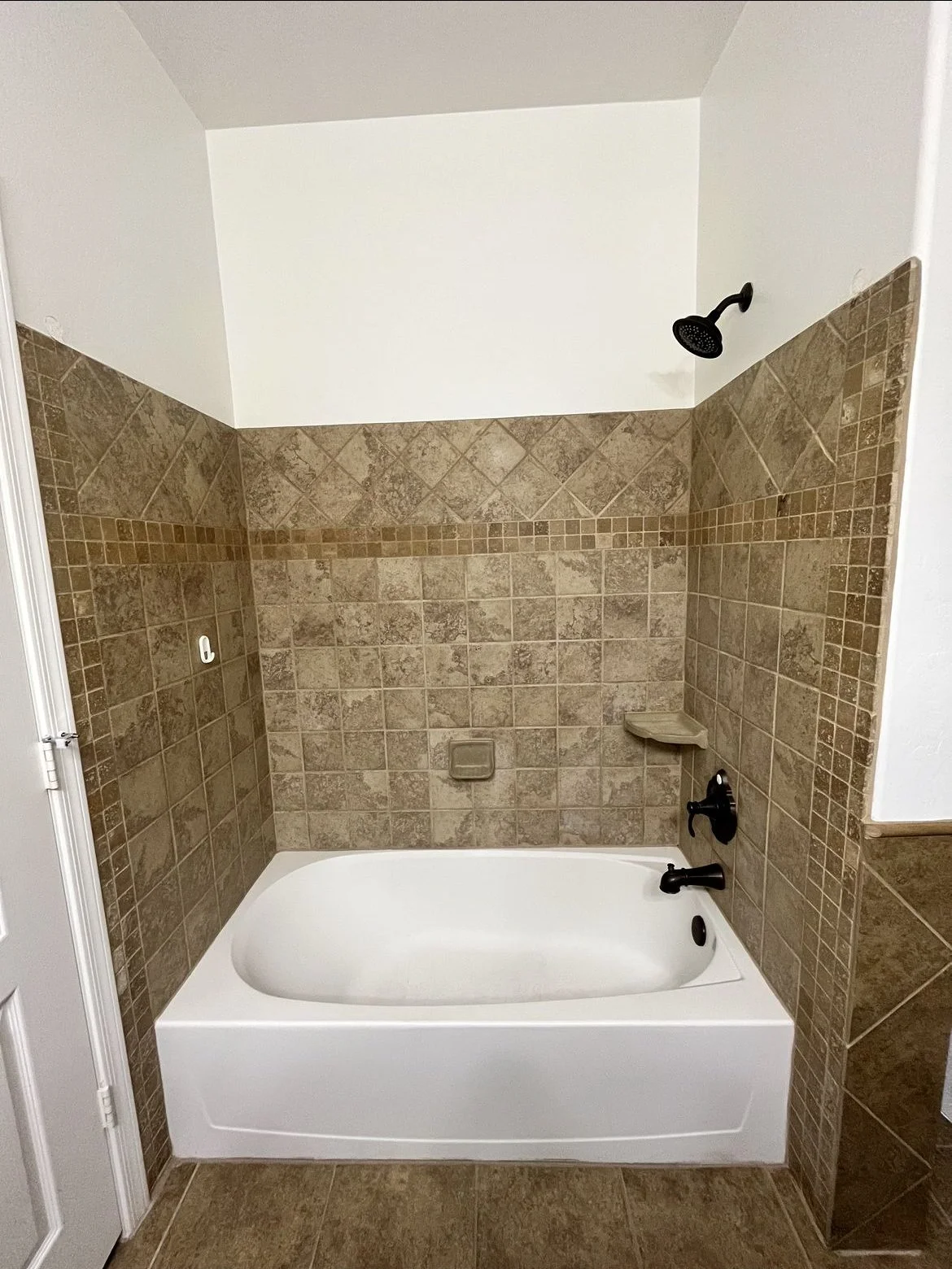 White alcove bathtub with brown stone tile surround and oil-rubbed bronze shower fixtures