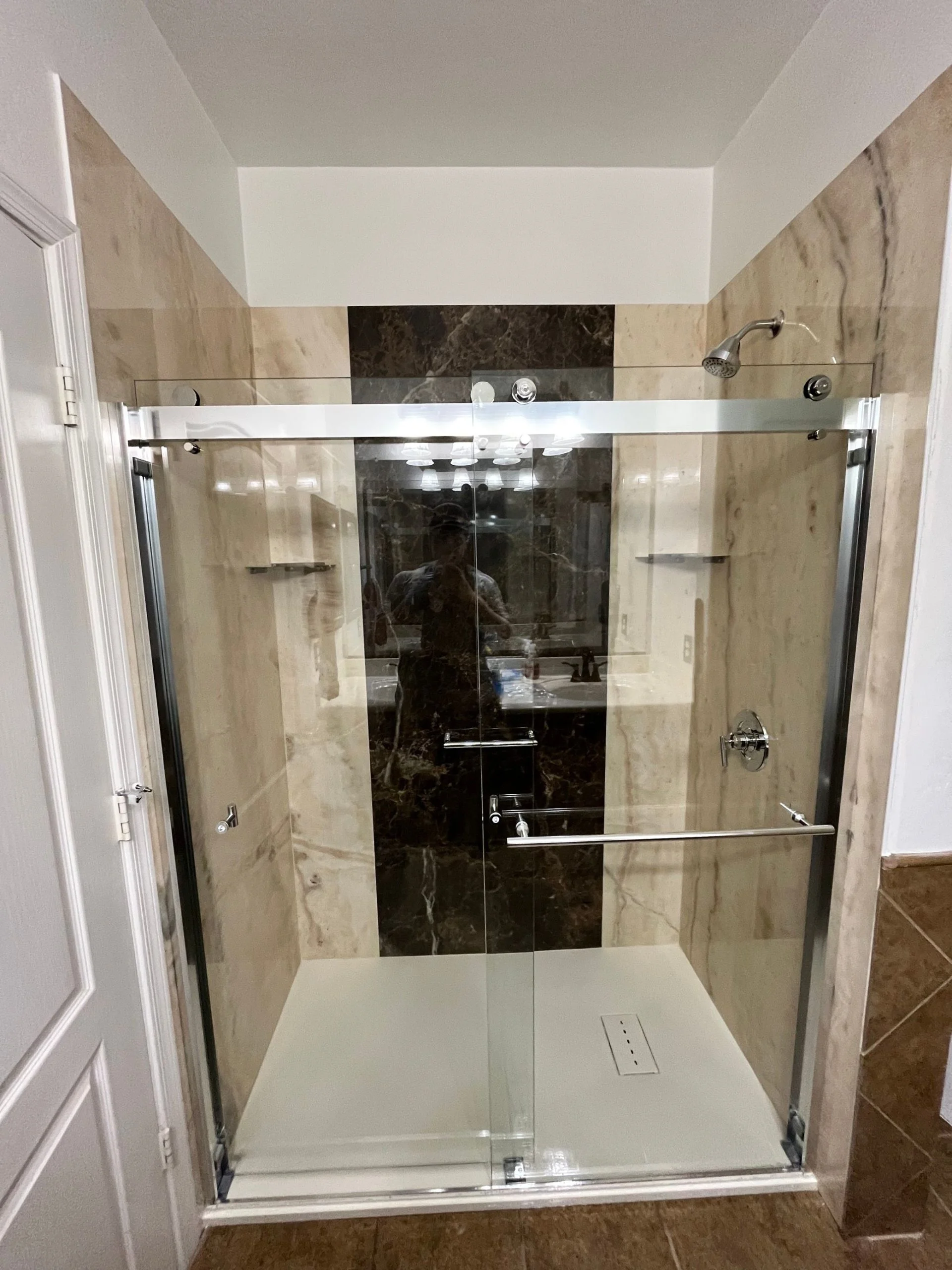 Modern walk-in shower featuring glass sliding doors and contrasting tan and dark brown marble tiles.