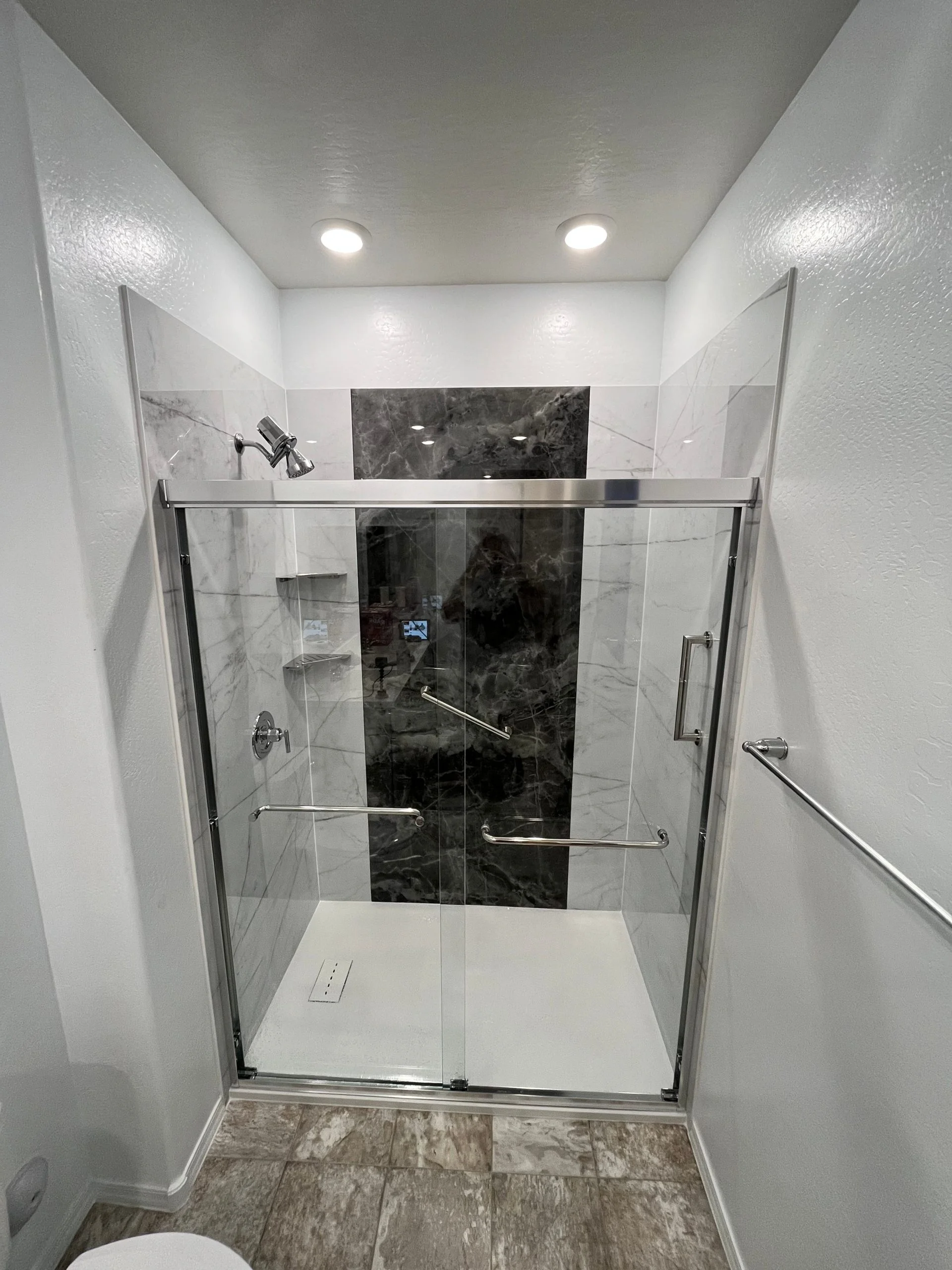 Modern walk-in shower featuring white marble walls with a dark gray marble accent strip and sliding glass doors.