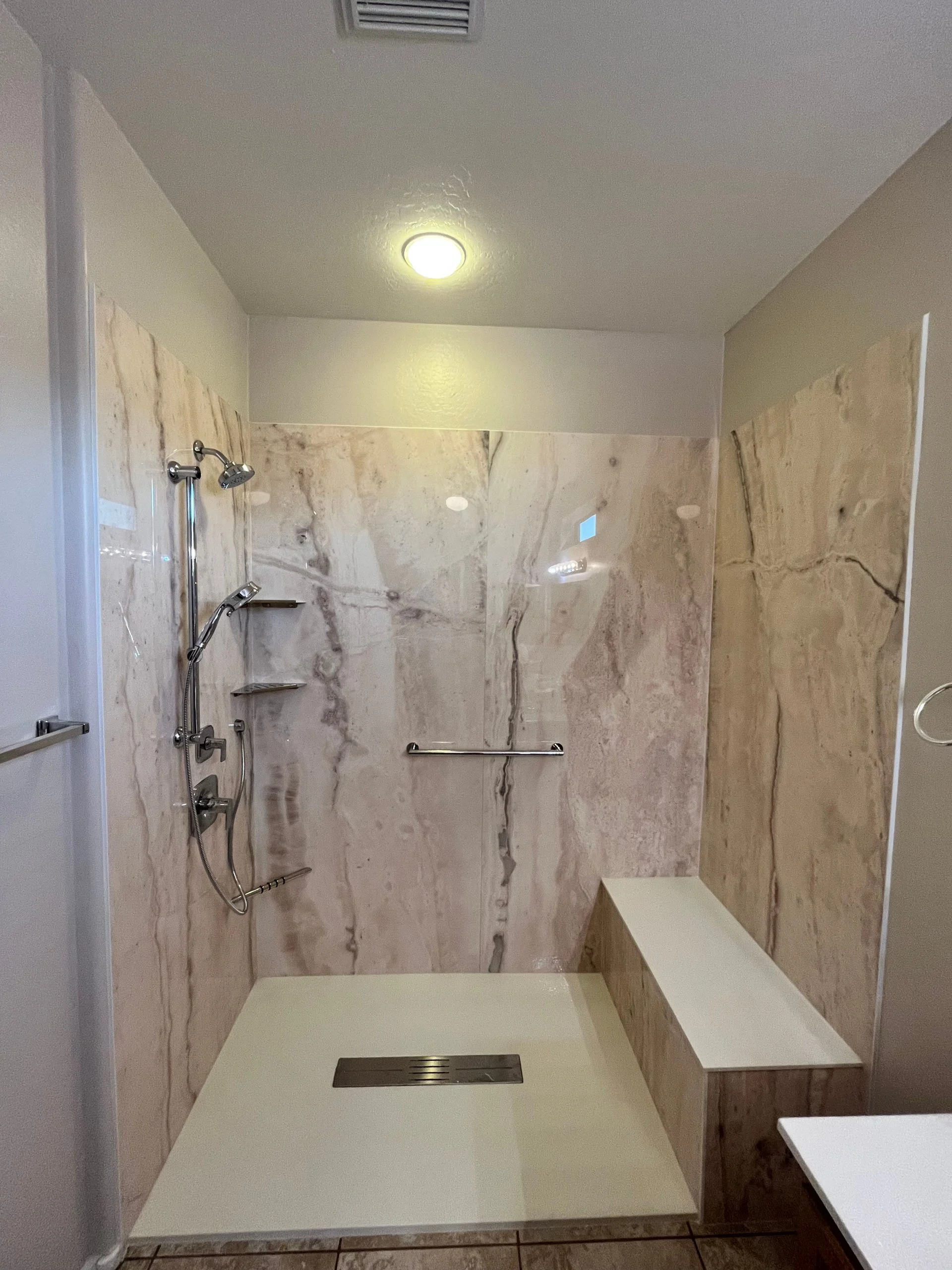 Modern walk-in shower featuring marbled stone-patterned wall panels, a built-in bench, and chrome fixtures.