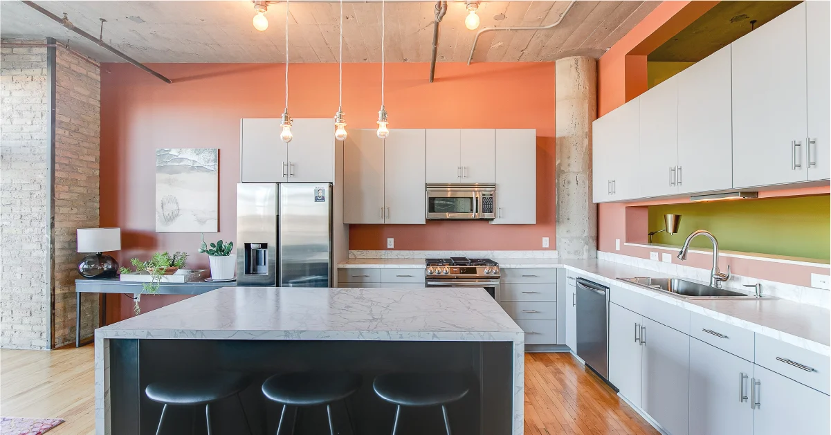 Modern industrial kitchen featuring grey cabinetry, marble countertops, and terracotta walls with exposed concrete ceilings.