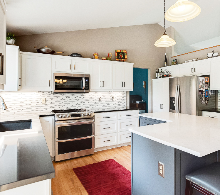 Modern kitchen featuring white upper cabinets, gray island, and a geometric white tile backsplash.