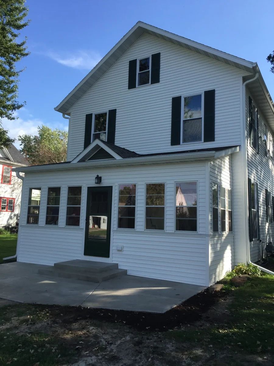 A newly renovated two-story house with white vinyl siding, black shutters, and multiple replacement windows featuring black trim installed on the front facade.