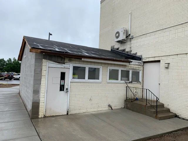 A small commercial building entrance with a white-painted exterior and metal roof addition to a larger industrial structure.